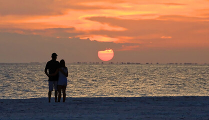 Beach lovers watch the sunset over Sanibel Island from Fort Myers Beach, Florida, USA.