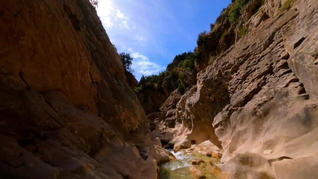 FPV drone backwards shot along yellow canyon, with people walking by blue water