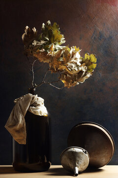 Composizione verticale con bottiglia, imbuti, foglie di quercia; still life su fondo scuro