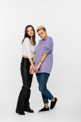 full length of smiling lesbian couple holding hands on grey background.