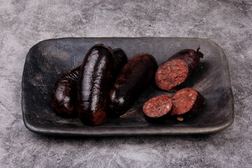 fried whole and sliced blood sausage on a black clay plate, gray stone background,Traditional...
