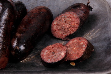 fried whole and sliced blood sausage on a black clay plate, gray stone background,Traditional Latvian blood sausages