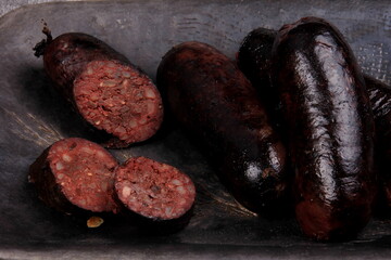 fried whole and sliced blood sausage on a black clay plate, gray stone background,Traditional Latvian blood sausages