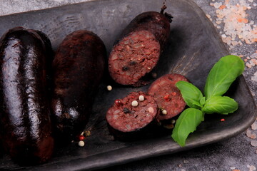 fried whole and sliced blood sausage on a black clay plate, gray stone background,Traditional Latvian blood sausages