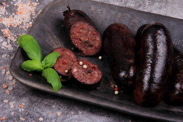 fried whole and sliced blood sausage on a black clay plate, gray stone background,Traditional...