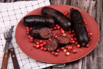 Baked blood sausage on a red plate decorated with red cranberries, Traditional Latvian blood...