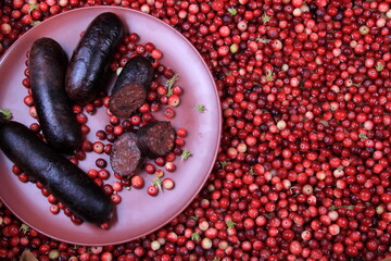 Baked blood sausage on a red plate decorated with red cranberries, Traditional Latvian blood...