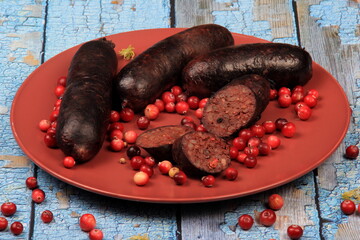 Baked blood sausage on a red plate decorated with red cranberries, Traditional Latvian blood...