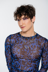 brunette queer model in long sleeve shirt and silver necklaces isolated on grey.
