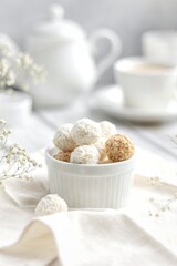 White and beige candies lie in a plate on a white background, next to it is a coffee pot and a cup of coffee