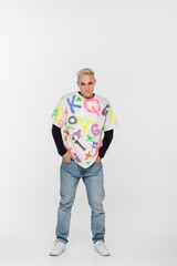 Fototapeta premium young gay man in alphabet print t-shirt standing with hands in pockets of jeans on grey background.