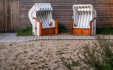 Obraz na płótnie Canvas Zwei schöne, helle Strandkörbe mit Strandsand vor einer Holzwand in schönem Ambiente.