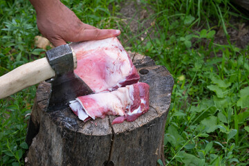 An ax in the hands of a butcher cuts lamb ribs on a stump.