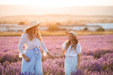 Beautiful stylish mother walk with kid girl daughter holding hands together in looming flower lavender field over nature outdoor. Look at each other. Motherhood. Spring season. Childhood.