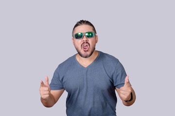 A man with long hair and wearing sunglasses acting tough and macho, pointing to the camera while yelling. Isolated on a gray background. - obrazy, fototapety, plakaty