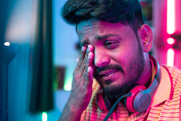 close up shot of exhausted or tired gamer rubbing his eyes while playing video game during late night - concept of gaming addiction and health care © WESTOCK