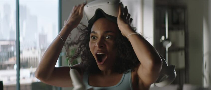 Portrait of excited African American female taking off her VR virtual reality metaverse headset at home after finishing playing