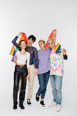full length of joyful friends of diverse identity holding lgbtq flags on grey background.