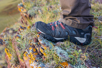 Close-up of man's foot in a sneaker on rock in the mountains. Hiking and trekking background. Active leisure weekend or sports travel concept.
