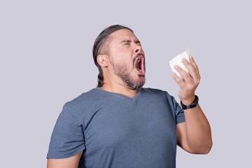 A man in his 30s is about to sneeze into a tissue paper. Triggered by an allergy or a cold.