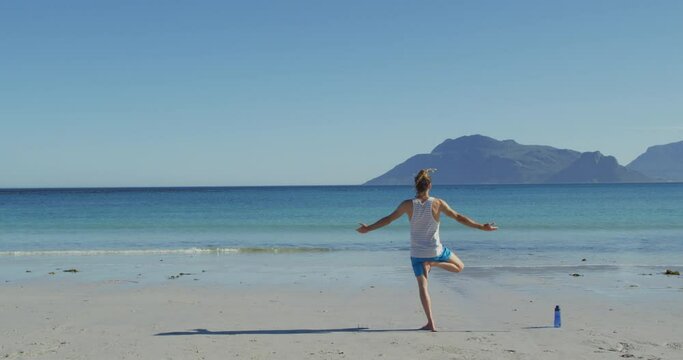 Video of rear view of caucasian man with dreadlocks practicing yoga standing on sunny beach