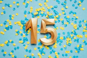 Number 15 fifteen golden celebration birthday candle on yellow and blue confetti Background....