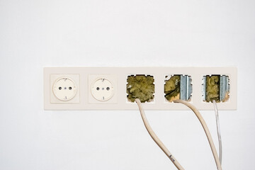 White electrical socket with switches and protruding wires on a white wall