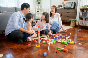 Asian family with children playing and building tower of colorful wooden toy blocks in living room at home, Educational game.