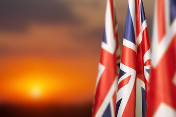 National flags of United Kingdom on a flagpole on sunset sky background. Lowered UK flags. Background with place for your text. - obrazy, fototapety, plakaty