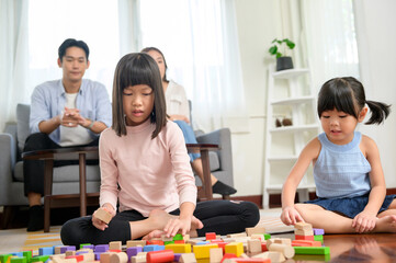Asian family with children playing and building tower of colorful wooden toy blocks in living room at home, Educational game.