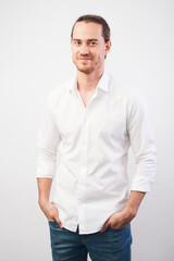 Portrait of young successful young man in white shirt, smiling holding hands in pockets over gray wall. Confidence and business concept.