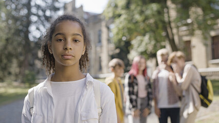 Group of school kids laughing at unhappy biracial girl, bullying problem