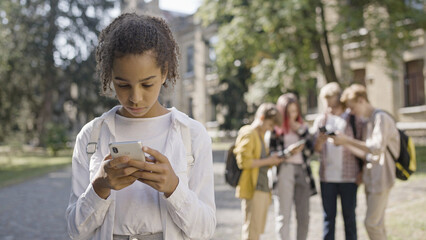 Sad African American girl suffering from social media bullying from group of school children