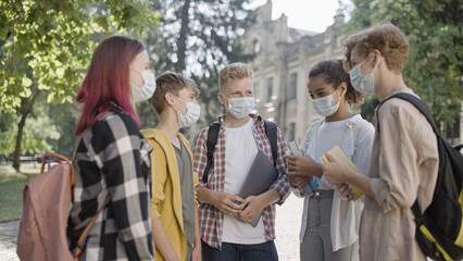 College students in protective face masks discussing classes on campus, education amid covid-19...