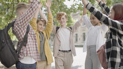 Cheerful multiethnic friends raising hands up, celebrating success, teambuilding