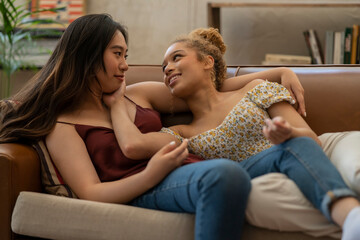 couple of multiracial young lesbian women, caressing on the sofa at home