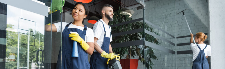 interracial women washing glass entrance in office near man with floor scrubber machine, banner.