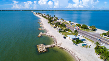 Aerial Drone Close Up of the Causeway Bridge in Sanibel, Florida with the Bay and a Preserve in the Foreground and the Gulf of Mexico in the Background Featuring a Blue Sky and Blue Water - obrazy, fototapety, plakaty