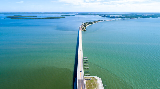 Aerial Drone Close Up of the Causeway Bridge in Sanibel, Florida with the Fort Myers Bay in the Foreground and the Gulf of Mexico in the Background Featuring a Blue Sky and Blue Water