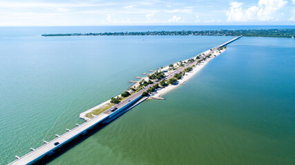Fototapeta na wymiar Aerial Drone View Showing the Causeway Bridge in Sanibel, Florida with the Bay and a Preserve in the Foreground and the Gulf of Mexico in the Background Featuring a Blue Sky and Blue Water