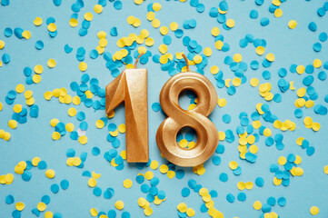 Number 18 eighteen golden celebration birthday candle on yellow and blue confetti Background. eighteen years birthday. concept of celebrating birthday, anniversary, important date, holiday - obrazy, fototapety, plakaty