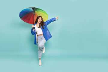 Young Asian woman wearing raincoat and holding rainbow umbrella isolated on green background, In...