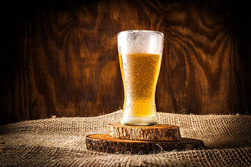 Glass with beer and foam on dark rustic wooden background and sack background
