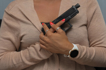 A pistol in female hands at the chest, close-up photo.