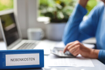 Symbolfoto hohe Nebenkosten für Mieter - Frau sitzt zu Hause am Schreibtisch und überprüft die...