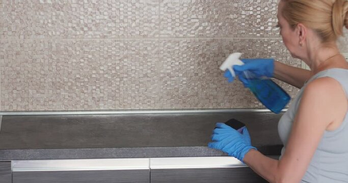 Girl in blue gloves cleans the kitchen countertop