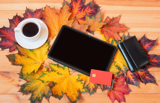 Tablet, purse, plastic card, cup of coffee and autumn maple leaves on desk. Autumn sale concept.