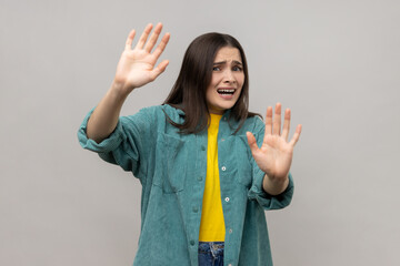 Portrait of scared young adult dark haired woman gesturing stop with palms and looking surprised...