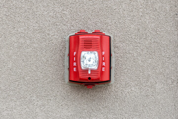 Red fire alarm siren with flashing light strobe isolated on gray cement wall outdoor. Fire safety.