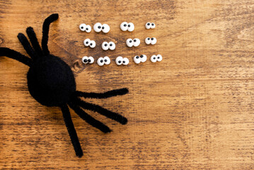 Blank black felted spider near many pairs of eyes made of polymer clay by hand on a wooden background